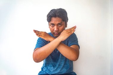 Mavi gömlekli bir adam kollarını çapraz yapıp beyaz bir arka plana karşı açık bir el hareketi yapar.