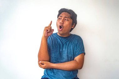 Mavi gömlekli bir adam işaret parmağıyla yukarı işaret ediyor. Bir fikri olduğunu gösteriyor. Diğer eli dirseğini destekliyor, düşünceli bir duruşu vurguluyor.