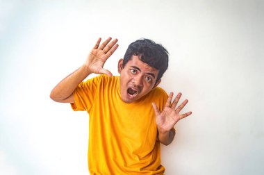 Turuncu gömlekli bir adam sürpriz bir hareketle poz veriyor, iki elini de açık avuçlarıyla beyaz arka plana doğru kaldırıyor. Bu resim şoku ya da şaşkınlığı vurgular