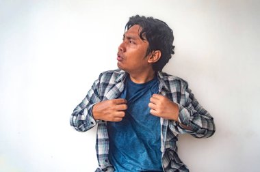 Ekose gömlekli ve mavi tişörtlü bir adam vücudundan gömleğini çekiyor. Bu da sıcak ya da rahatsız olduğunu gösteriyor. Düz beyaz arka plan onun jestini vurguluyor.