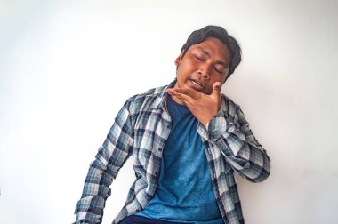 Ekose gömlekli ve mavi tişörtlü bir adam dilini ağzının çatısına bastırarak miyavlama tekniğini gösterir. Düz beyaz arka plan jesti açıkça vurguluyor