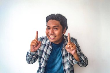 Ekose gömlekli ve mavi tişörtlü bir adam her iki işaret parmağını yukarı kaldırarak neşeli bir jest yapıyor. Düz beyaz arka plan jesti vurguluyor