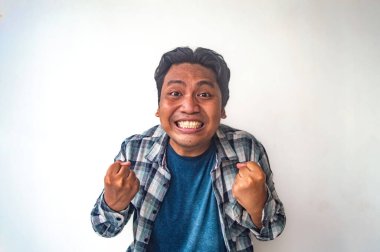 Ekose gömlekli ve mavi tişörtlü bir adam her iki yumruğunu da sıkıyor. Başarılı bir hareket ya da beyaz bir arka plana karşı zafer işareti olarak. Görüntü bir başarı ve neşe anı yakalar.