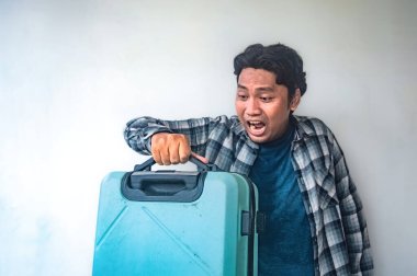 Ekose gömlekli bir adam sürpriz bir jest içeren mavi bir bavul tutuyor. Görüntü beklenmedik bir tepkiyi yakalar, seyahat, macera veya sürpriz temalı içerik için uygun hale getirir