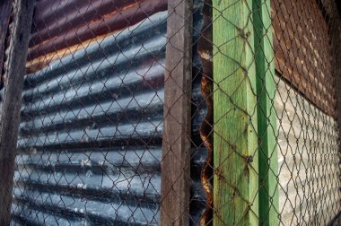 Oluklu metal levhalar, tel örgüler ve yıpranmış ahşap kirişler birleşerek desenli, endüstriyel bir köşe oluşturuyor. Bu resim ayrışma ve katmanlı materyalleri vurgular, grunge veya soyut için mükemmeldir