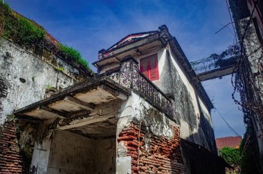 Endonezya 'da eski, yıpranmış bir bina. Paramparça tuğlaları ve mavi gökyüzünün altındaki boyaları. Tarihsel mimari yeşil bitkilerin yaşını ve ihmalini gösteriyor
