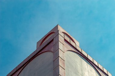 Açık mavi gökyüzüne karşı ince kırmızı kemerli elementlerle bir binanın çarpıcı mimari ayrıntıları modern çizgiler ve klasik eğrileri vurguluyor.