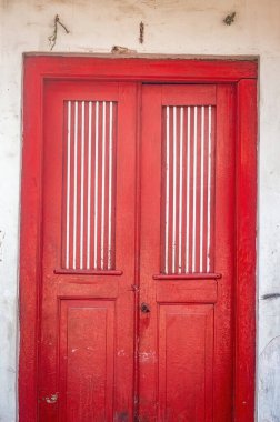 Geleneksel hoparlörlü panelleri olan canlı kırmızı ahşap kapı, kırsal beyaz bir duvara dayanıyor. Çarpıcı bir mimari detay