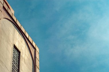 Bir binanın dokulu dış cephesinin minimalist mimari görüntüsü kemerli detaylar ve geniş bir açık mavi gökyüzüne karşı desenli bir pencere.