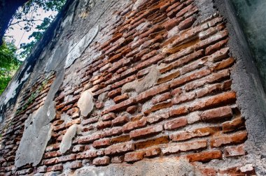 Endonezya 'da yıpranmış tuğla duvarın düşük açılı görüntüsü, yeşil yapraklara karşı eski dokuları ve kırsal cazibeyi gösteriyor.