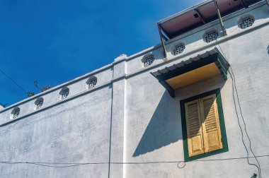 Temiz mavi gökyüzünün altındaki eski bir binanın güzel mimari ayrıntıları klasik kepenkleri ve eşsiz yuvarlak duvar deliklerini sergiliyor.
