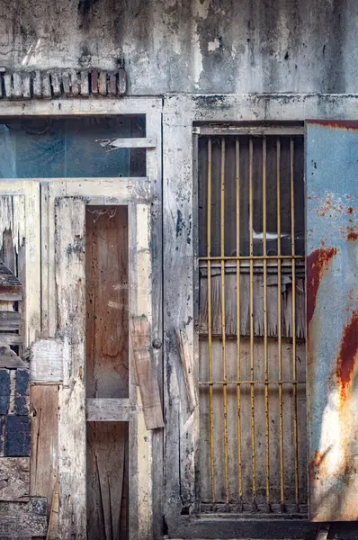 Aşırı derecede yıpranmış ve sıkıntılı ahşap bir kapı paslı bir metal panel ve güvenlik parmaklıklarıyla, aşırı kentsel bozulmayı gösteriyor. Terk edilme, grunge, yoksulluk ya da tarihi harap teması için.