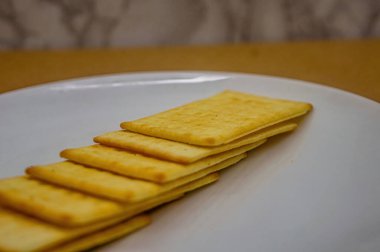 Beyaz bir tabakta düzgün bir sıraya dizilmiş birkaç altın, dikdörtgen krakerin yakın bir yan görüntüsü. Gıda reklamları veya atıştırmalık içeriği için ideal