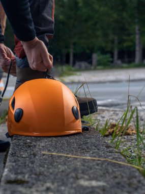 Dağ tırmanışçısı, tırmanmaya hazırlanıyor. Deri botlarını turuncu bir kask ile bağlıyor. Kopya alanı.