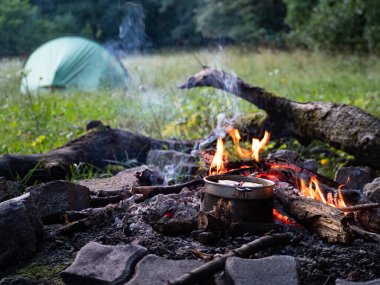 Kamp ateşinde kamp yaparken arka planda çadır var, kimse yok.