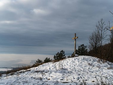 Güneş, karlı bir dağın tepesindeki ahşap bir çarmıhta parlıyor. Kış manzarası, bulutlu hava, gri gökyüzü dini kefareti.