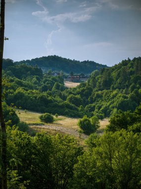 Gün batımında dağlarda bir orman çayırındaki binalar. Bulutlu gökyüzü ormanı yol çalıları.