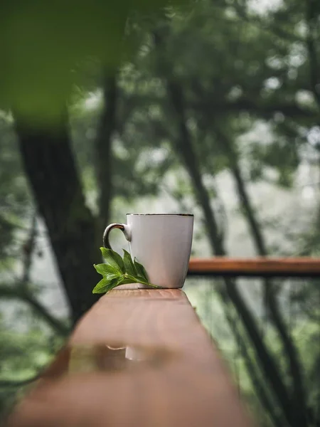 White coffee tea mug with tea leaves coffee leaves on a forest balcony porch in the morning, summer nature getaway vacation