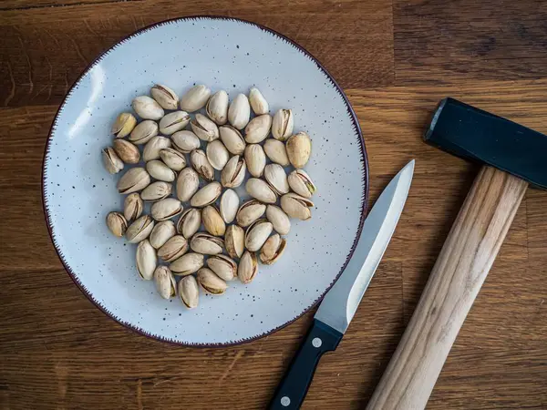Tabaktaki şam fıstıklarının yukarıdan aşağı aranjmanı çekiç ve bıçakla kırılmak için hazırlanıyor. Kırsal ahşap masa arka planı.