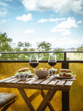 Evde öğle yemeği için bir masa, balkonda hamburger, salata ve şarap, evde iki kişilik romantik bir randevu, ev yapımı yemek.