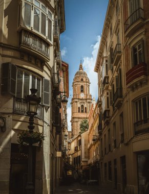Malaga Katedrali Saat Kulesi, evler, Endülüs, İspanya, yaz tatili, mavi gökyüzü, güneş ışığı arasında dar bir sokaktan görünüyor.