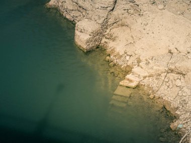 An old stone staircase going under water in a lake into the sea as seen from above, in Spain, Andalusia