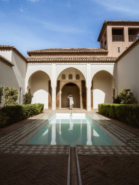 İç havuz avlusu Malaga, Endülüs 'teki Alcazaba Kalesi' nden Patio de la Alberca 'nın önünde belirgin Fas kemerleri ve sütunları önünde duran bir kadın turist duruyor..