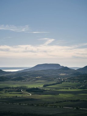 Mavi gökyüzü ve arka planda dağlar olan güzel bir manzara. Dağlar ağaçlarla kaplı ve çimenler yemyeşil. Balatonfelvidek, Balaton, Badacsony, Macaristan 'da huzur ve sükunet hakim.