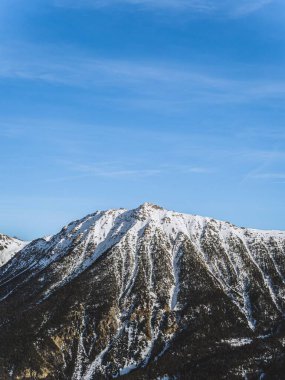 Briancon 'daki Serre Chevalier zirvesinin göz kamaştırıcı manzarası, açık mavi gökyüzüne karşı. Engebeli dağ manzarası kışın Fransız Alplerinin güzelliğini gözler önüne seriyor..