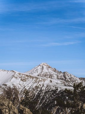 A stunning view of the snow-covered Serre Chevalier peak in Briancon, set against a clear blue sky. The rugged mountain landscape showcases the beauty of the French Alps in winter. clipart