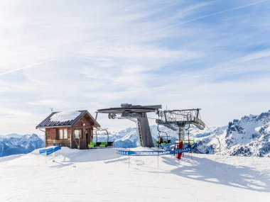 Fransız Alpleri 'ndeki Serre Chevalier tatil köyünde bir kayak kaldırma istasyonu. Arkasında ahşap bir kulübe ve karla kaplı tepeler var. Sahne, dağlarda açık ve güneşli bir günü yakalar..
