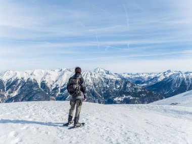 Sırt çantalı yalnız bir yürüyüşçü Briancon, Fransa 'da karlı bir dağda duruyor, açık mavi gökyüzünün altındaki geniş panoramik zirvelere hayran..