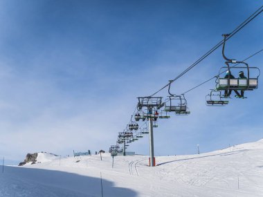 Serre Chevalier 'de açık ve güneşli bir kış gününde kar yamaçlarında kayakçıları taşıyan bir teleferik. Mavi gökyüzü ve karla kaplı manzara kayak ve snowboard yapmak için mükemmel bir sahne oluşturuyor..