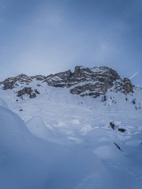 Briancon, Fransa 'daki Serre Chevalier Kayak Tesisi' nde nefes kesici bir kış sahnesi. Kar kaplı yamaçlar, engebeli tepeler ve açık mavi gökyüzünün altında dağınık çam ağaçları sergileniyor..