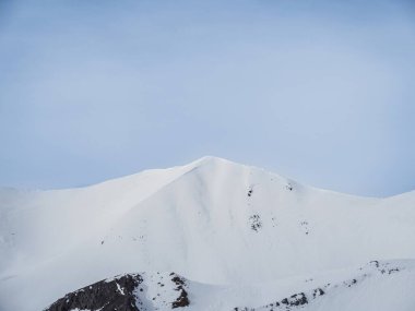 Temiz mavi gökyüzüne karşı el değmemiş, karlı bir dağ zirvesi yükselir. Pürüzsüz yamaçlar ve el değmemiş kar sakin ve görkemli bir alp manzarası yaratır..