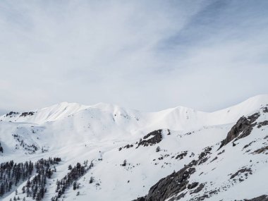 Montgenevre, Fransa yakınlarındaki sakin, karlı bir dağ manzarasında temiz bir kış gökyüzü altında el değmemiş yamaçlar, engebeli tepeler ve dağınık ağaçlar yer alıyor..