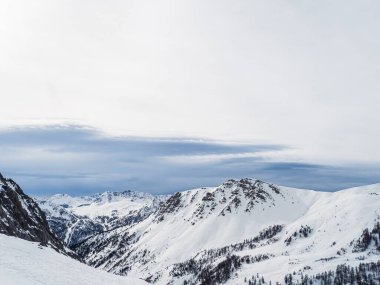 Montgenevre, Fransa yakınlarındaki sakin, karlı bir dağ manzarasında temiz bir kış gökyüzü altında el değmemiş yamaçlar, engebeli tepeler ve dağınık ağaçlar yer alıyor..