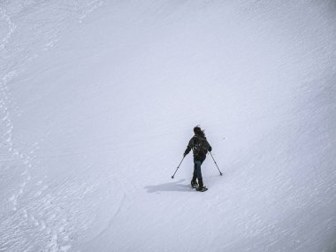 Karlı bir dağ zirvesi bulutlu gri bir gökyüzünün altında uzun duruyor. Yumuşak, el değmemiş yamaçlar ve sessiz tonlar sakin ama dramatik bir alp sahnesi yaratır..