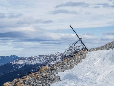 Rusted barbed wire near WW2 fortifications on Mont Chaberton, France, with snow-covered peaks and a dramatic cloudy sky. Highlights history amid rugged alpine scenery. clipart