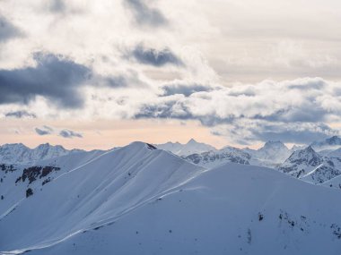 A golden hour view from Mont Chaberton near Briancon, France, showcasing snow-covered peaks and a dramatic sky with vibrant clouds. The serene alpine valley enhances the breathtaking scene. clipart