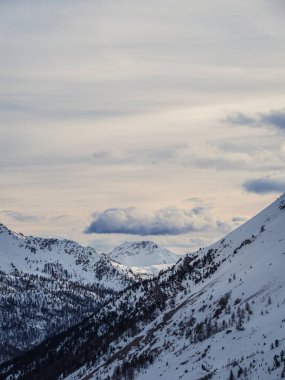 Orman yamaçları ve dramatik bulutlu bir gökyüzünün altındaki uzak tepelerle çevrili karlı bir vadi. Montgenevre, Fransa yakınlarında yakalandı..