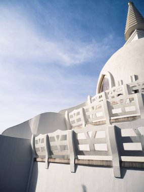 Parlak mavi gökyüzüne karşı, karmaşık detaylarıyla serin, beyaz bir stupa. Minimalist mimari, yapının zarafetini ve ruhsal özünü vurgular..