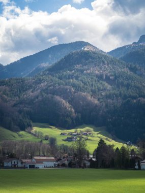 Bavyera 'daki Aschau im Chiemgau' nun pitoresk bir manzarası, hareketli yeşil çayırlar, antika bir köy, ve dramatik bulutlu bir gökyüzünün altındaki orman dağları..