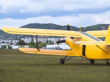 A classic yellow biplane parked on a grassy airfield with a cityscape and mountains in the background, showcasing vintage aviation and aircraft design. clipart