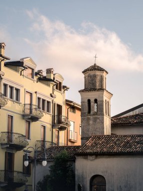 İtalya 'nın Grado kentindeki tarihi binaların büyüleyici bir manzarası, haçı ve pastel renkli cepheleri olan bir köy kilise kulesi. Altın gün batımı ışığı zarif balkonları ve çatıları güçlendirir..