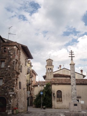 İtalya 'nın Grado şehrinde sakin bir meydanda kırsal bir kilise, uzun bir taş sütun ve parçalı bulutlu bir gökyüzünün altındaki ortaçağ binaları bulunuyor. Tarihi kasaba hayatına barışçıl bir bakış..