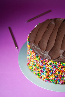 Lezzetli çikolatalı ganache doğum günü pastası. Pembe arka planda renkli serpiştirilmiş.