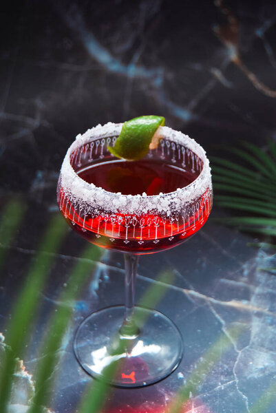 Red alcoholic cocktail, lime garnish, salted rim, marble background, ornate glass, fairy lights