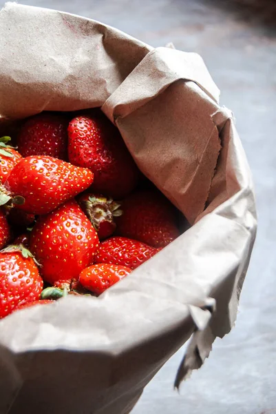 Juicy red organic strawberries from the farmers market, in a paper bag on a marble counter, focused