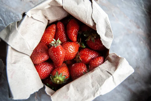 Juicy red organic strawberries from the farmers market, in a paper bag on a marble counter, focused